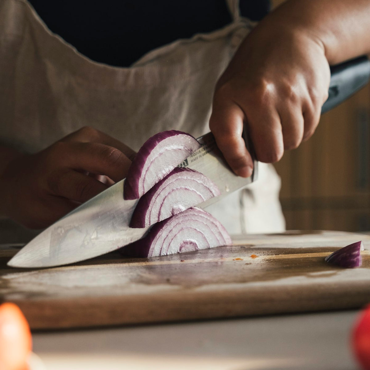 Hands slicing a red onion on a wooden cutting board